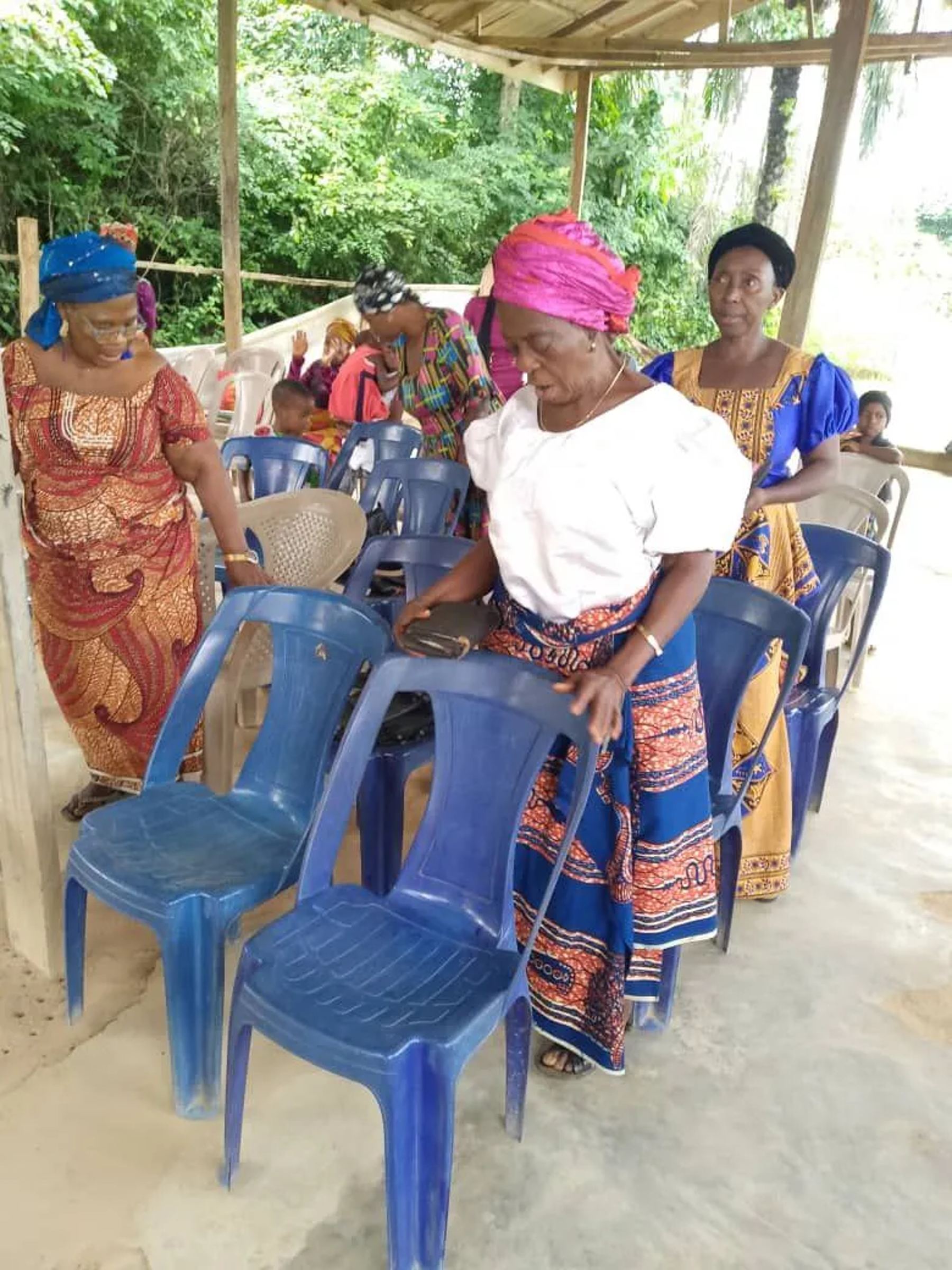 Women in colourful wrappers and head ties finding their seats among the blue chairs