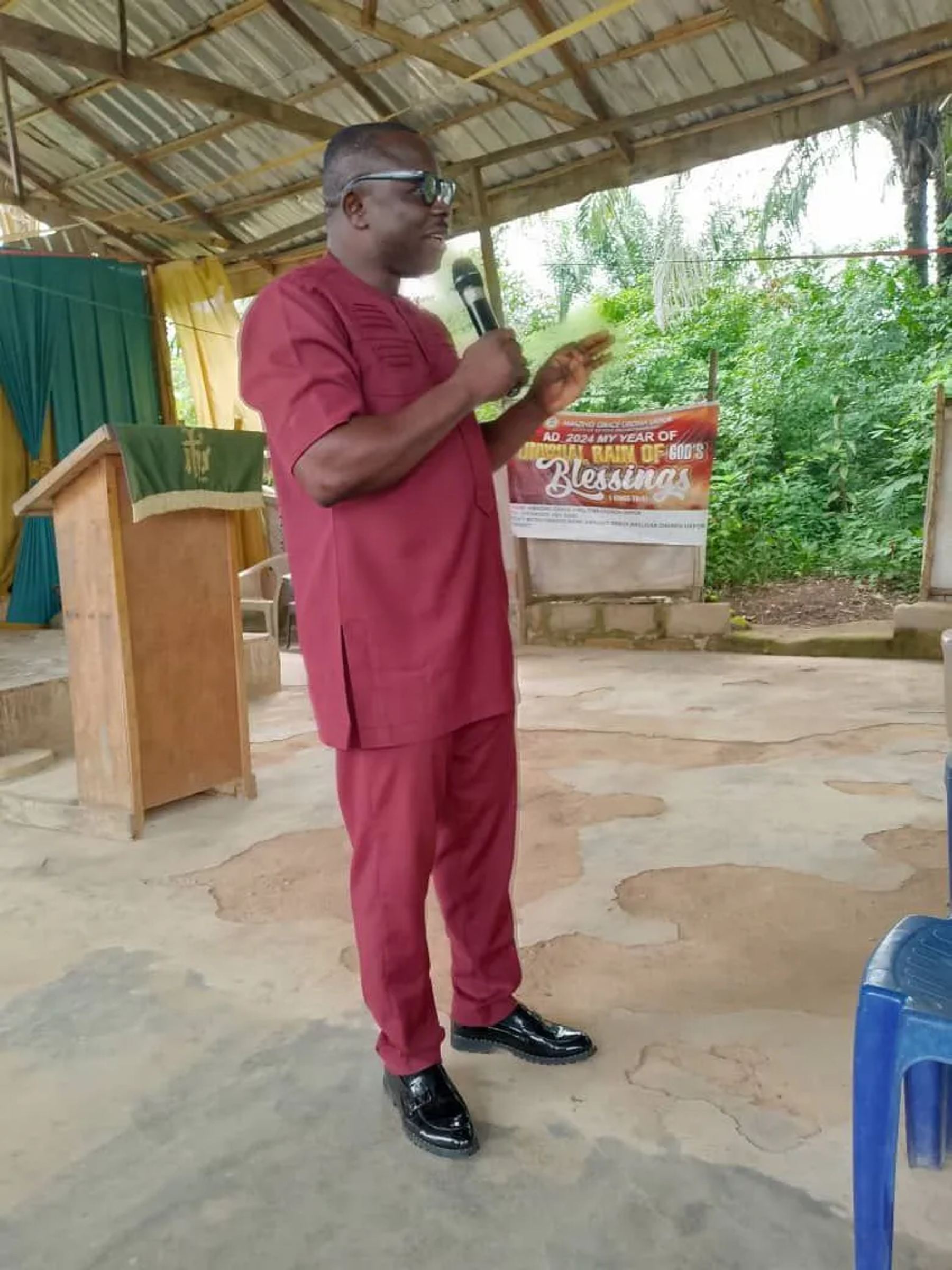A minister in red holding a microphone and reading notes beside the wooden pulpit