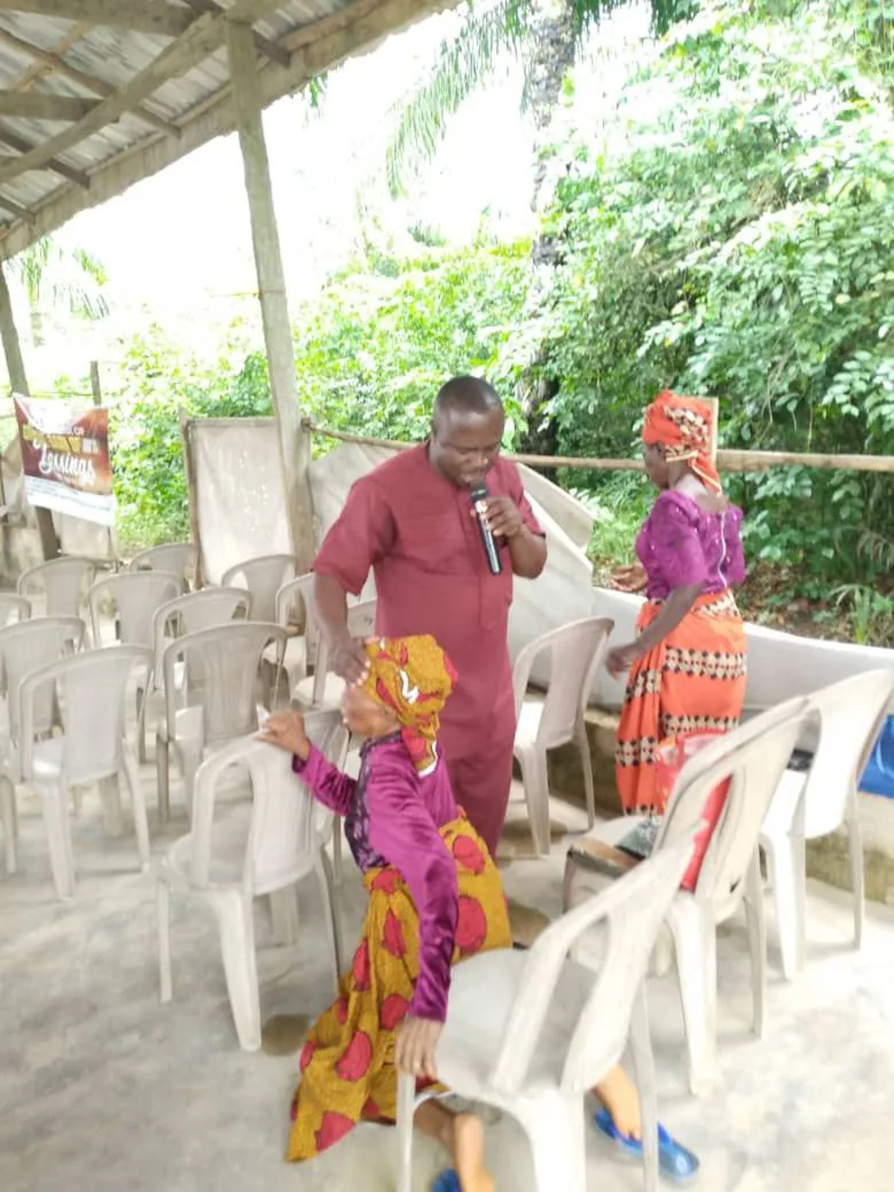 A minister with a microphone praying over a kneeling woman between rows of white chairs