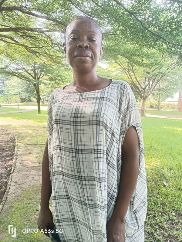 A speaker in a long checked dress standing outside under the trees